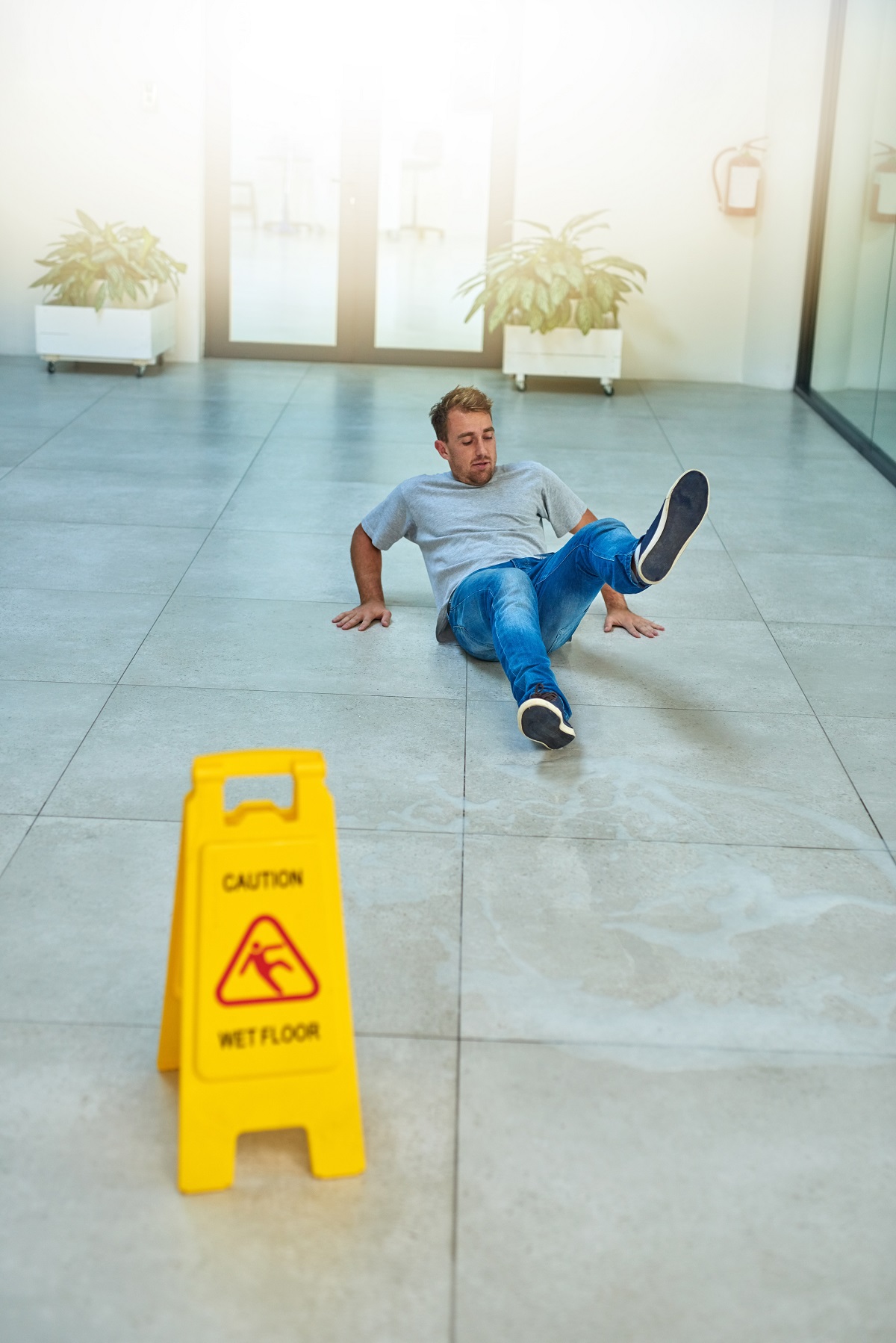 A man on the ground after a fall by a "Wet Floor" sign