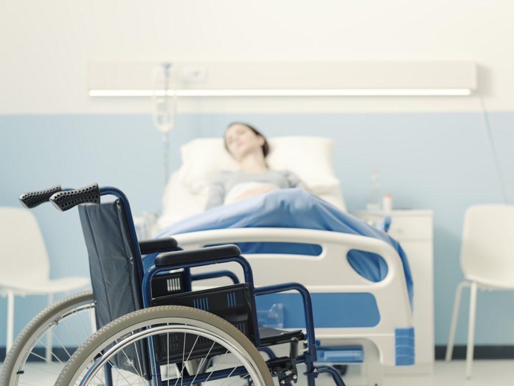 A woman lying in a hospital bed near a wheelchair