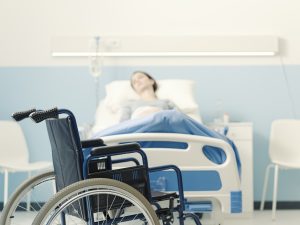 A woman lying in a hospital bed near a wheelchair