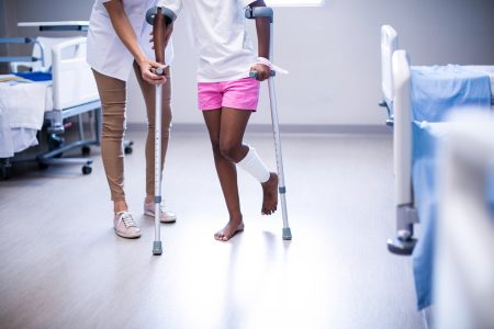 An injured person using crutches with the help of a nurse