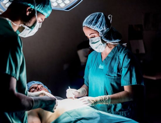A surgeon and assistant conducting surgery on an unconscious patient